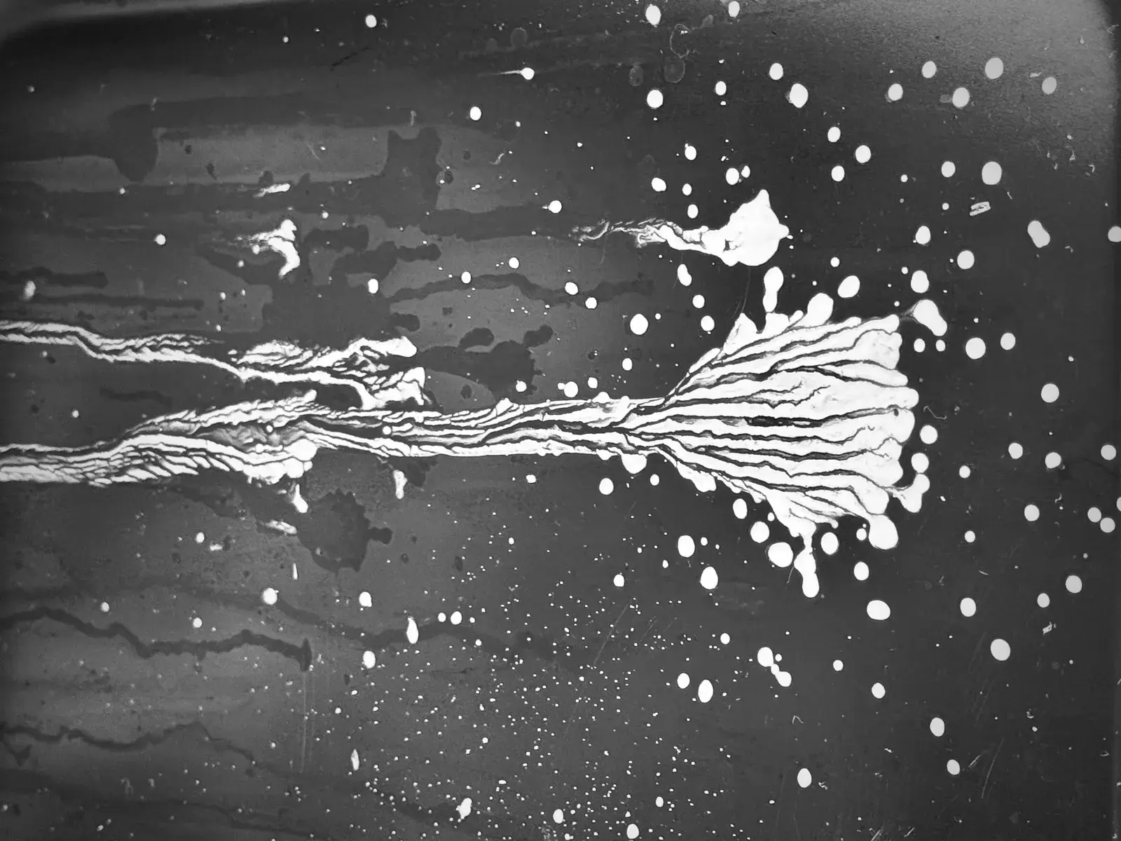 Streaks and spatters of white spreading across a dark field, like spilled ink.