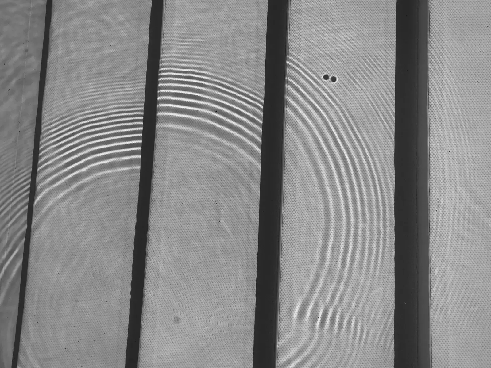 Concentric ripples of light spreading across a striped, ridged fabric surface, like circles rippling out on water.